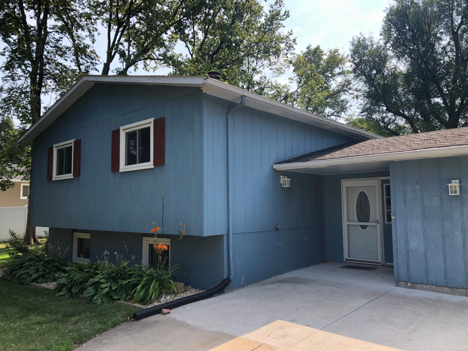 Split-level home before repainting, with faded medium-blue siding, red shutters, and dated trim